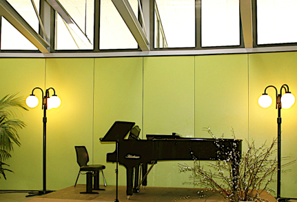 Schwarzer Klavierflügel umgeben von zwei Straßenlaternen in einem geschlossenen Raum